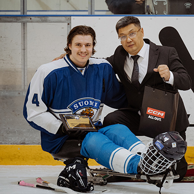 Nemo Pajula poseeraa ottelun parhaan pelaajan palkinnon ja palkitsijan kanssa Astanan 2025 B-sarjan MM-turnauksessa Paraleijonien pelipaidassa, ilman kypärää jääkiekkokelkassaan jäällä.